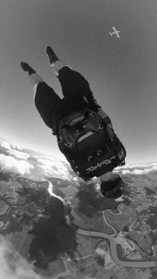 Skydiver in freefall wearing a JYRO rig, with a plane and river valley below